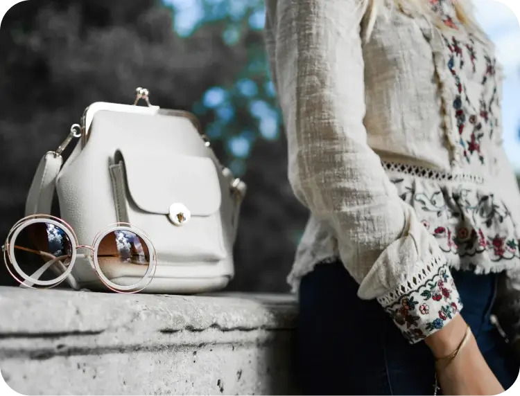 A Woman Leaning Against A Wall With Sunglasses And A Purse